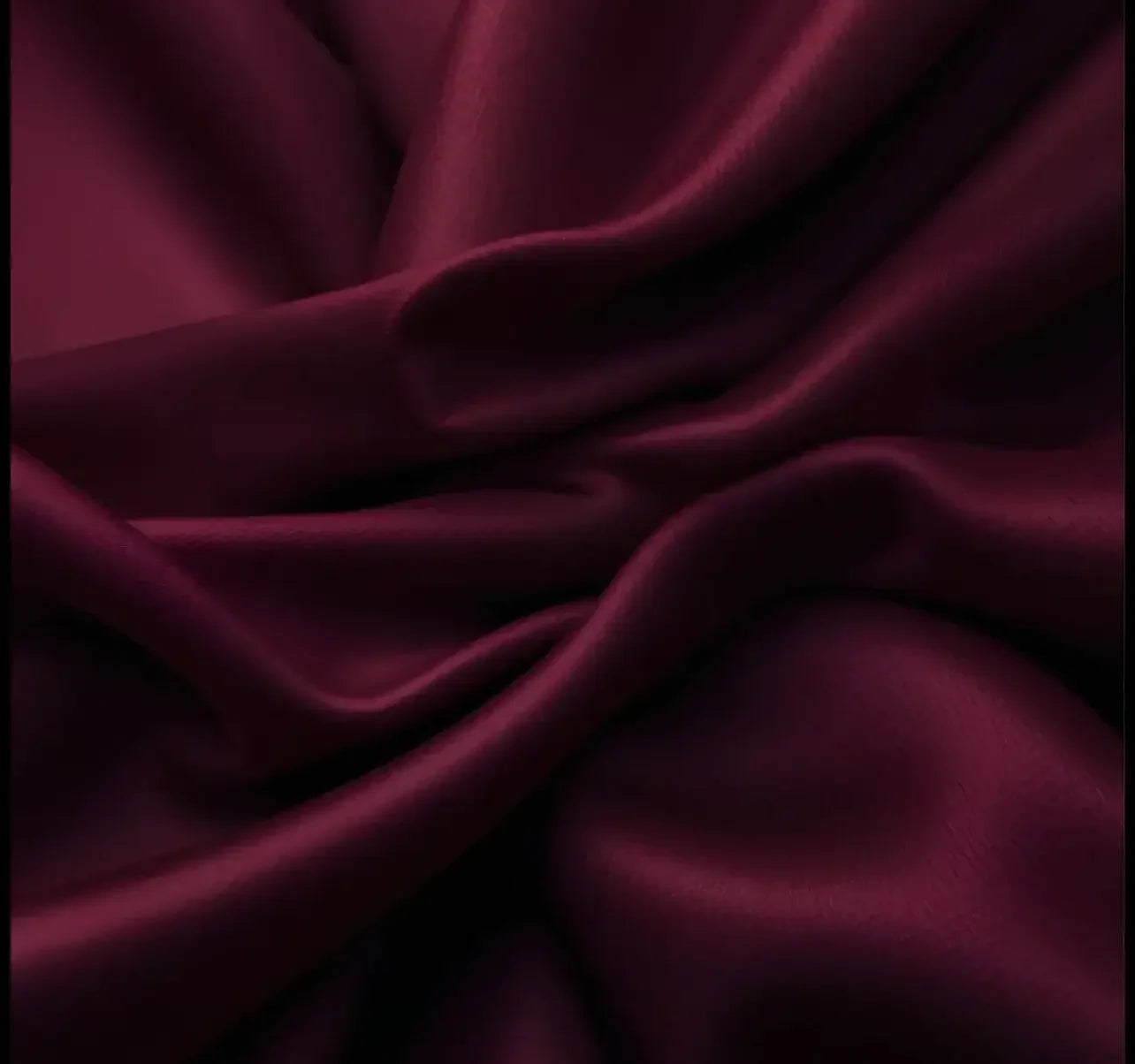 Close-up of deep burgundy silk fabric with smooth, flowing folds and shiny texture