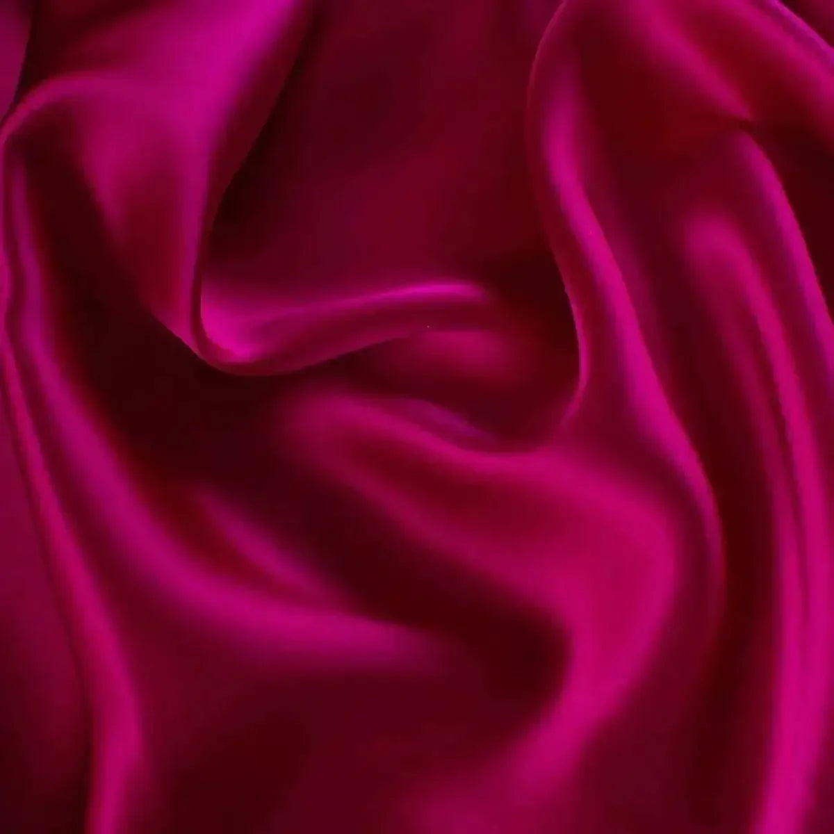 Close-up of smooth fuchsia pink silk fabric with flowing folds and a glossy finish